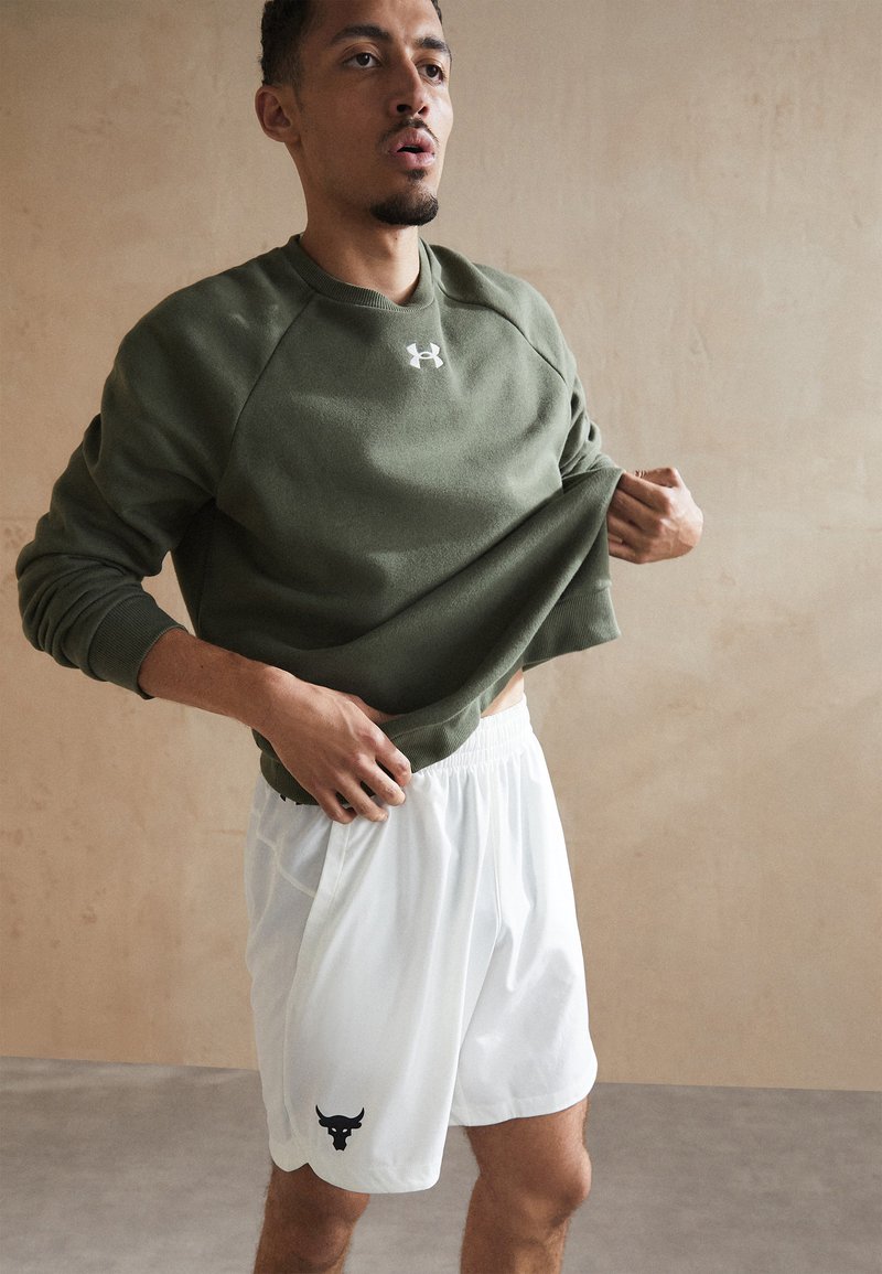 Grüner Sweatshirt mit einem gerippten Rundhalsausschnitt und einem weißen Logo, kombiniert mit weißen Shorts, die ein schwarzes Bullen-Graphic zeigen. Einfaches, sportliches Design.