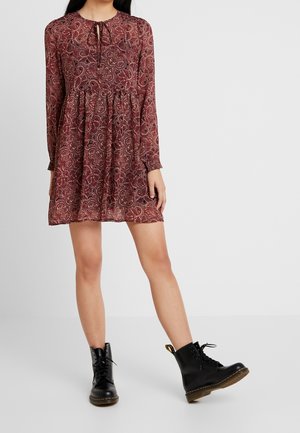 Robe à motifs cachemire bordeaux avec manches longues et col noué. Portée avec des bottines en cuir noir à lacets et semelle épaisse.