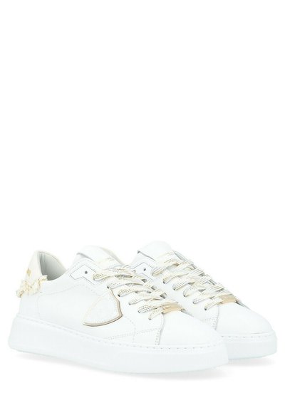 Sneaker bianchi in pelle con una texture liscia, dettagli dorati sui lacci e sul lato, e una suola bianca spessa. Presentano dettagli cuciti e un logo.