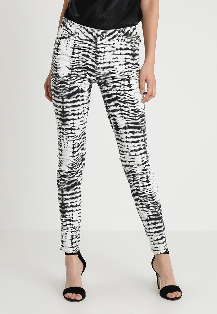 Modèle féminin portant un pantalon skinny en tie-dye noir et blanc avec un haut noir sans manches et des sandales à talons hauts noires, debout.
