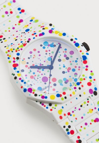 Montre en silicone colorée avec un bracelet blanc, présentant un cadran rond orné de points multicolores, et des aiguilles des heures et des minutes bleues.