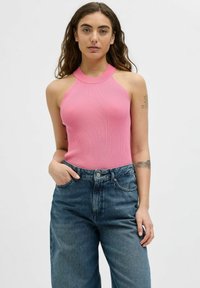 Rožinė banguota tankų viršutinė dalis su kaklo juosta, derinama su aukštu juosmeniu mėlynomis džinsinėmis kelnėmis. Modelis su natūraliais banguotais plaukais ir tatuiruotėmis.