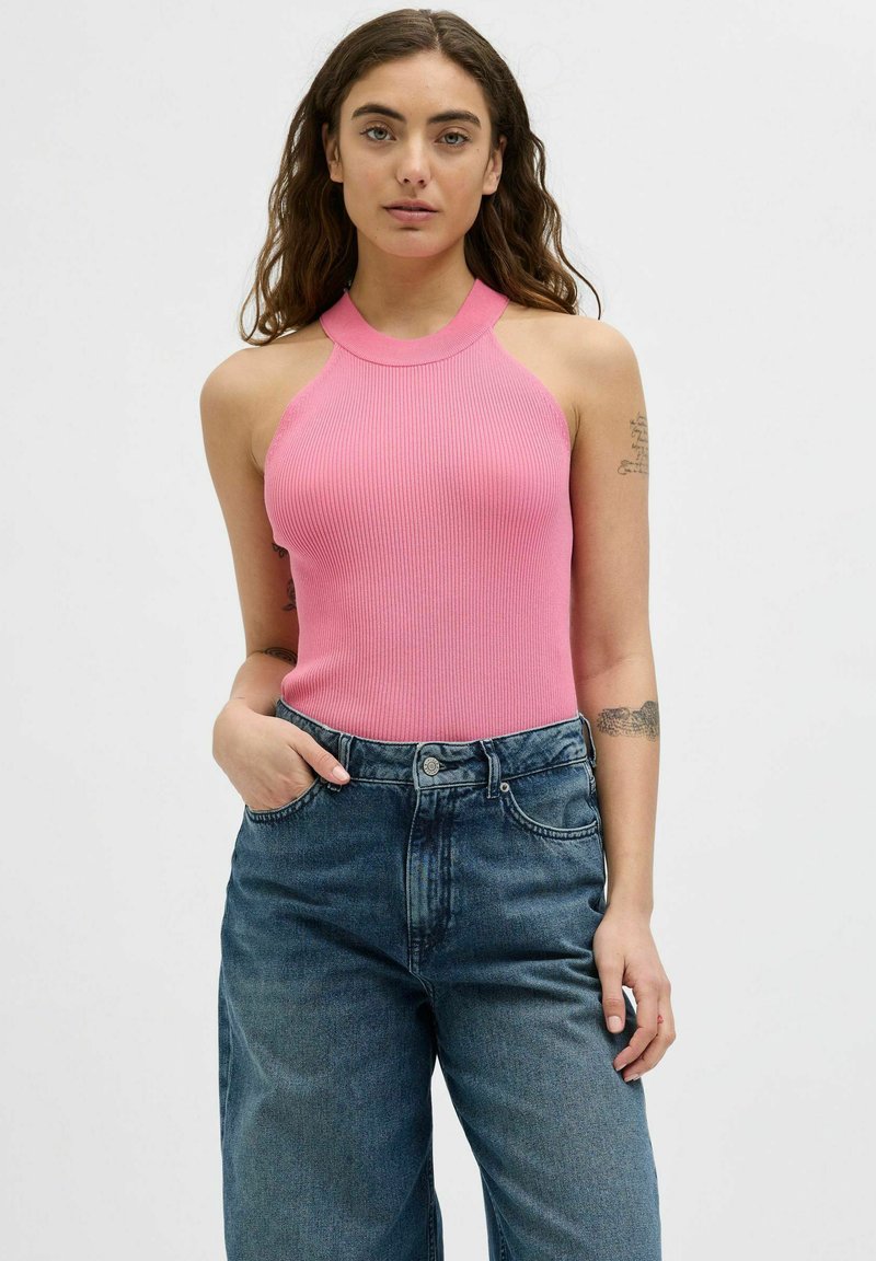 Rožinė banguota tankų viršutinė dalis su kaklo juosta, derinama su aukštu juosmeniu mėlynomis džinsinėmis kelnėmis. Modelis su natūraliais banguotais plaukais ir tatuiruotėmis.