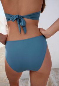 Modra kopalna dvodelna obleka z zavezanim bandeau zgornjim delom in visokim pasom. Gladka tekstura in minimalni šivi povečajo udobje in prileganje.