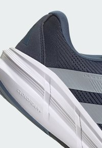 Nahaufnahme der Ferse eines blauen Sportschuhs mit strukturiertem Stoffoberteil und weißer Sohle mit eingeprägtem "CLOUDFOAM".