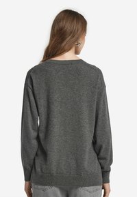 Grauer Strickpullover mit lockerer Passform, gerippten Bündchen und Saum. Weicher Stoff, runder Halsausschnitt und minimalistisches Design ohne Verzierungen.