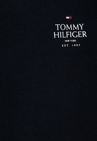 Camiseta marinera de algodón, con un logotipo de marca bordado en blanco que dice "TOMMY HILFIGER", "NEW YORK" y "EST. 1985". Textura suave.