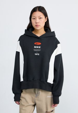 Felpa nera con accenti laterali bianchi, caratterizzata da un logo Nike arancione ben visibile e testo. Realizzata in un tessuto morbido con una vestibilità comoda.