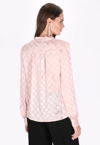 Lyserød bluse med en gennemsigtig finish, med prikm�ønster, lange ærmer og plisseret detalje bagpå. Skræddersyet pasform med rund kant.
