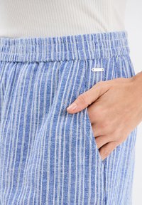 Blauwe en witte gestreepte broek met elastische tailleband en zijzakken, voorzien van een gestructureerde stof en een metalen logo-accent.