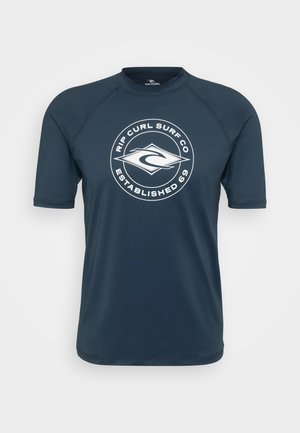 Κοντομάνικο, σκούρο ναυτικό rash guard φτιαγμένο από ελαφρύ ύφασμα, με λευκό κυκλικό λογότυπο που αναγράφει "Rip Curl Surf Co. Ιδρύθηκε το 69."