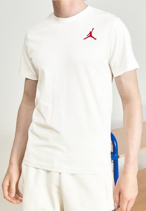 T-shirt à manches courtes de couleur crème, en coton, avec un logo Jumpman rouge brodé sur le côté gauche de la poitrine.