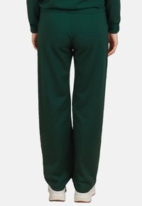 Groene, wijde sweatpants met een gladde textuur; elastische tailleband; gecombineerd met witte schoenen.