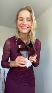 Mauve high-heeled shoes with a glossy finish and pointed open-toe design, held in a hand. Smooth texture with a price tag attached.