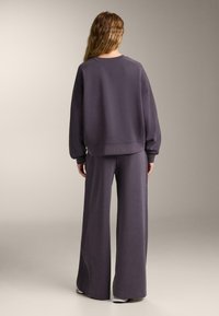 Felpa viola e pantaloni a gamba larga realizzati in un tessuto morbido. La parte superiore ha una vestibilità ampia e dettagli a coste, mentre i pantaloni presentano un taglio pulito e dritto.