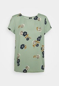 Zelená blůza s krátkým rukávem se květinovým potiskem v námořnické modré, bílé a hnědé barvě. Vyrobena z měkké, lehké tkaniny s kulatým výstřihem.