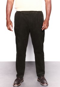 Pantalon en velours côtelé vert foncé à coupe droite, avec poches avant et texture lisse, assorti à des chaussures en cuir marron.