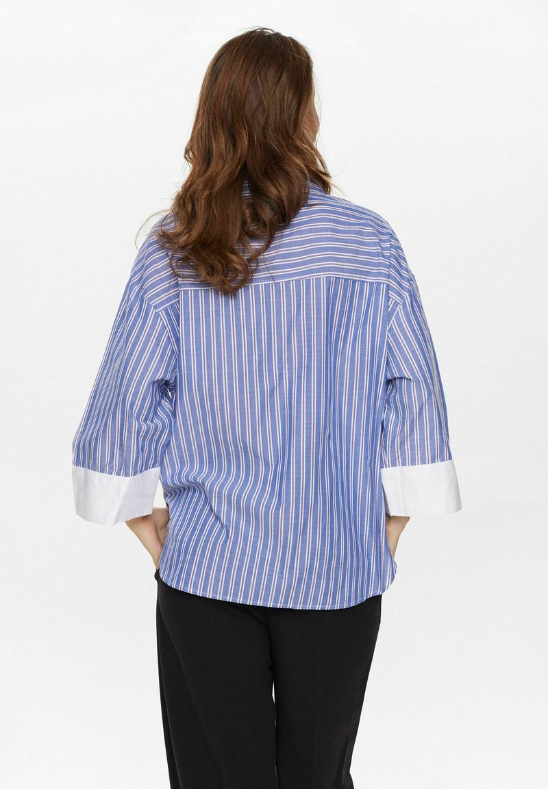 Camicia a righe blu e bianche con maniche a tre quarti, caratterizzata da un polsino bianco. Design casual e vestibilità ampia. Tessuto leggero.