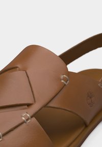 Καφέ δερμάτινο σανδάλι με φαρδιές λουρίδες, μεταλλικές λεπτομέρειες ραφής και σχέδιο slingback.