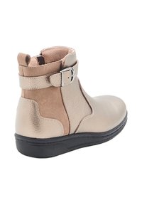 Botte de cheville en cuir avec une finition lisse beige et des accents en daim, une sangle ajustable et une semelle en caoutchouc noir.