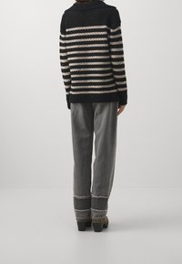 Gestrickter Pullover mit schwarzen und cremefarbenen horizontalen Streifen, ausgestattet mit einem breiten Kragen. Kombiniert mit grauen weiten Jeans und klobigen schwarzen Absatzschuhen.