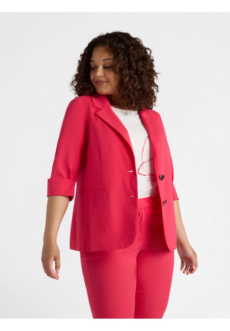 Blazer rosa con chiusura a un bottone, maniche a tre quarti e due tasche frontali, abbinato a pantaloni coordinati decorati con piccoli embellishments.