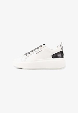 Witte lage sneaker met dikke zool, grijze veters, zwarte hielpatch en "SMITH X" branding aan de zijkant.