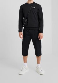Sudadera negra con el logo de EA7, combinada con pantalones capri negros y zapatillas blancas. Los accesorios incluyen un pequeño bolso cruzado negro.