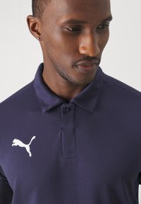 Marineblaues Polohemd mit strukturierter Oberfläche, ausgestattet mit einer Zwei-Knopf-Leiste und einem weißen Puma-Logo auf der linken Brust.