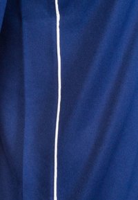 Dunkelblauer Stoff mit einer glatten Textur und einer kontrastierenden weißen vertikalen Naht, die in der Mitte verläuft. Einfaches und schlankes Design.