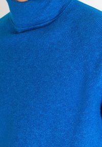 Pull à col roulé bleu, texture côtelée, coupe ajustée, léger brillant, avec un col haut et des détails de couture sur l'épaule.