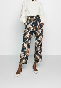 Flödande, högmidjade, vida byxor i marinblått med ett brunt och krämfärgat tropiskt lövmönster, med knyt-bälte och djupa sidofickor.