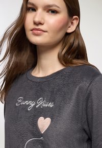 Felpa in fleece grigio scuro con ricamo "Bunny Kisses", scollo rotondo e una consistenza morbida. Presenta un design con cuore rosa e coniglio.