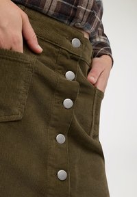 Gonna in velluto a coste verde oliva con bottoni a pressione in metallo lungo il lato, dettagli con tasca e tessuto strutturato.