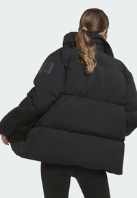 Juodas pūkinis švarkas su aukštu apykakliu, pasižymintis siuvinėtu dizainu ir Adidas logotipu kairėje petyje. Minkšta, stora medžiaga.