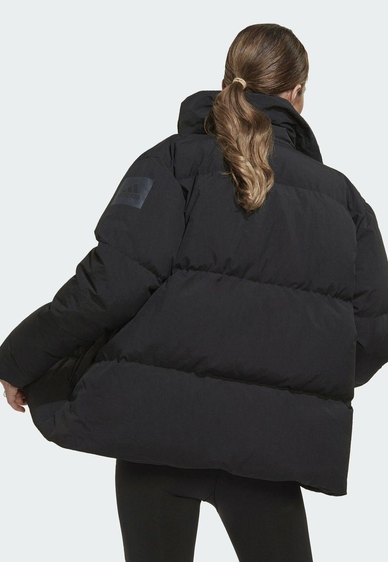 Schwarze Steppjacke mit hohem Kragen, ausgestattet mit einem gesteppten Design und einem Adidas-Logo-Patch auf der linken Schulter. Weicher, dicker Stoff.