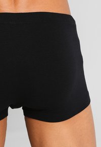 Boxers en coton noirs avec une coupe ajustée, présentant une texture lisse et une taille élastique. Design simple sans motifs ni logos.