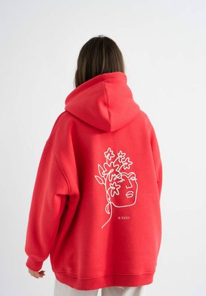 Rode oversized hoodie met een groot geborduurd gezicht en een bloemenontwerp op de achterkant. Gemaakt van zachte stof met een capuchon en geribbelde boorden.