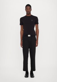 Tricou negru cu mânecă scurtă, guler rotund și un logo rotund, asortat cu pantaloni largi negri și mocasini. Design simplu, minimalist.