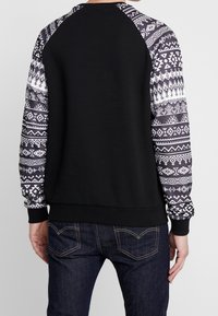 Felpa nera con maniche grigie e bianche a motivo, caratterizzata da design geometrici. Polsini e vita a costine, texture liscia.