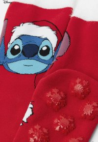 Rote Socken mit einem Cartoon-Charakter-Design, das Stitch mit einem Weihnachtsmannhut zeigt. Die Sohle ist mit erhabenen roten Schneeflocken-Noppen versehen.