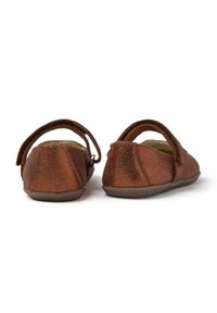 Zapatos de cuero marrón con un acabado texturizado, suelas planas y una correa ajustable en el tobillo. Punta redondeada y detalles de costura sutiles.