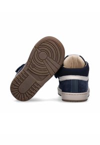 Marineblauwe sneakers van suede materiaal, met witte accenten, rubberen zolen en een getextureerd loopvlakpatroon. Voorzien van een klittenbandsluiting.