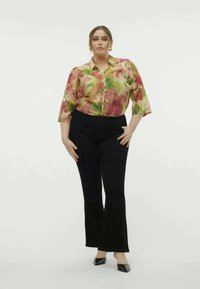 Floral button-up shirt with green and pink hues; paired with black flared pants. Model stands with hands on hips against a white background.
