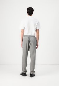 Grijze broek met een relaxte pasvorm, elastische tailleband en twee achterzakken, gecombineerd met een eenvoudig wit shirt met korte mouwen en zwarte schoenen.