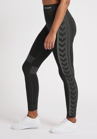 Leggings sportivi neri con vestibilità snella, motivo laterale testurizzato e accenti a pannello. Indossati con scarpe da ginnastica bianche.