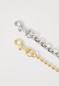 Două lanțuri metalice au un design cu inele de lanț din argint și un lanț cu bile din aur. Fiecare are un închizător distinct pentru o prindere sigură.