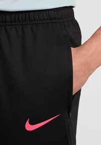 Pantalones cortos deportivos negros con un logo de Nike en rosa, cintura elástica y bolsillos laterales, que muestran una textura de tela suave y ligera.