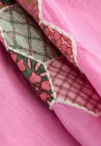 Tissu rose avec des motifs floraux et à carreaux, superposé avec des coutures blanches, créant un design texturé et coloré.