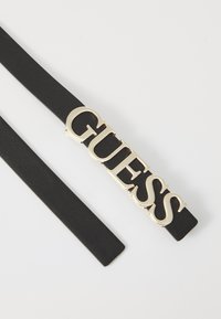 Čierny kožený opasok s výrazným zlatým kovovým logom "GUESS". Opasok má hladký povrch s elegantným, minimalistickým dizajnom.